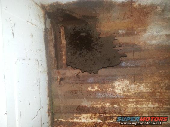 Rusted truck bed with large hole showing structural damage and white painted interior wall