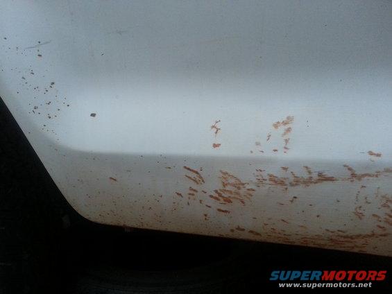Close-up of a white vehicle's lower body panel with dirt and mud splatters