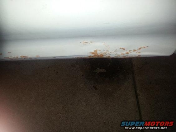 White vehicle lower body panel showing rust damage along the bottom edge