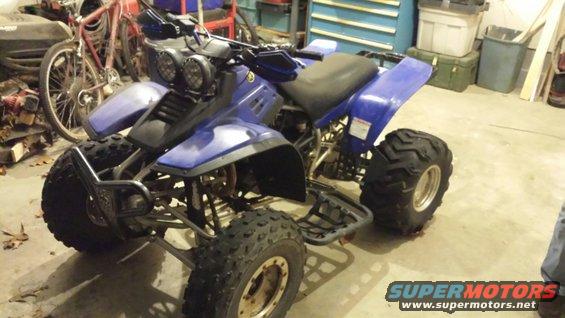 Blue ATV with dual headlights and aggressive tires parked indoors