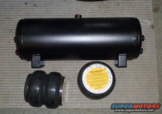 Black air suspension tank with two rubber bellows and a yellow instruction label