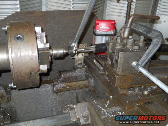 Lathe machine part being worked on with a wrench; red weather radio in background