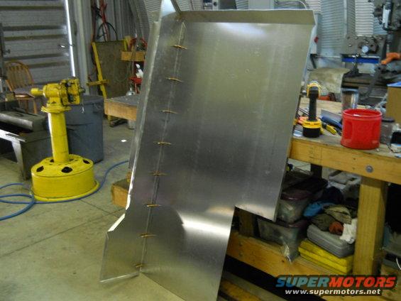 sheet metal piece with tack welds, in a workshop setting with tools and equipment