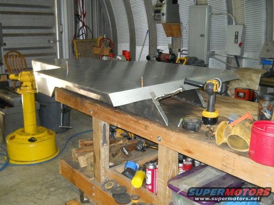 Metal sheet on workbench with tools, yellow vise, and Supermotors logo