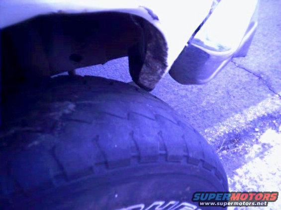 Close-up of a vehicle's tire and fender area, showing some rust and damage
