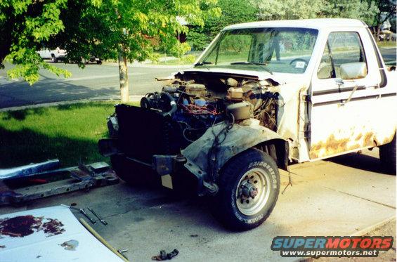 White Ford Bronco with front end disassembled, showing engine and rust on lower doors