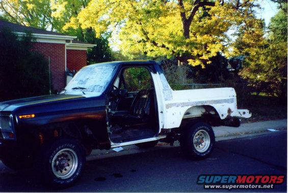 Ford Bronco with driver door open, dark blue front, white rear, parked on street