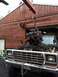 1979 Ford Bronco - An engine is being removed from a truck using an engine hoist in front of a wooden building.