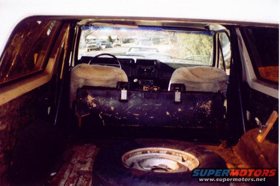 Interior view of a 1980s Ford Bronco, showing front seats, dashboard, and spare tire in the cargo area