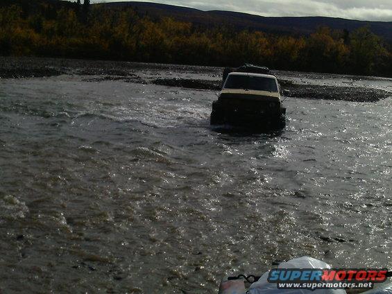 White SUV fording a river with trees in background