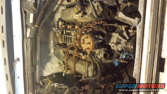 Engine compartment with engine and rusty chains draped over it. Some hoses and wiring are visible
