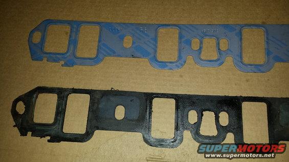 Two engine intake gaskets, one blue and one black and worn, against a brown surface