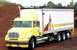 1999 Ford Crown Victoria - A yellow Freightliner box truck is parked on a dirt lot with a pile of brown material behind it.
