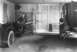 1909 Ford Model T - A man stands by a 1909 Ford Model T in a dealership garage, with a horse-drawn carriage also visible.