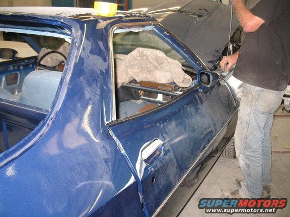Car door and interior of a blue vehicle being worked on, with a person in the background