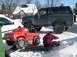 1986 Ford Bronco - A dark 1986 Ford Bronco is parked in the snow next to a red toy truck, with a person sitting on a sled nearby.