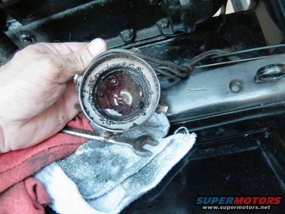 Hand holding a greasy, disassembled automotive component over a rag and engine parts