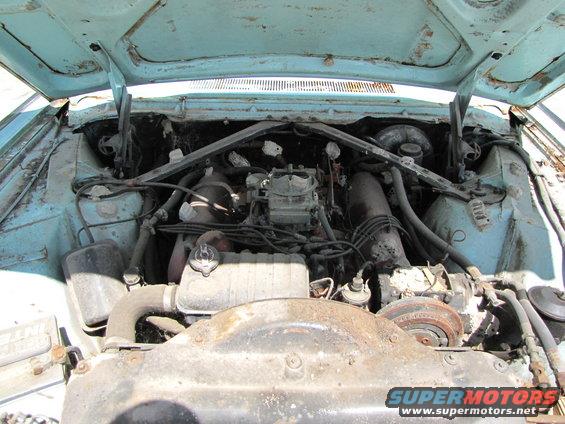 Engine bay of a light blue 1963 Ford Thunderbird, showing a V8 engine with a carburetor and extensive rust