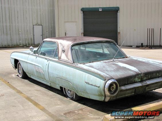 Old light blue car with a rusty roof parked outside a warehouse
