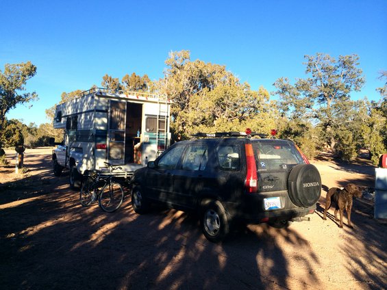 Black Honda CR-V with spare tire, rear view, parked next to a camper on a truck