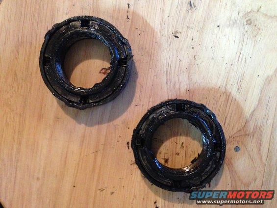 Two greasy, black bearing seals with visible wear and damage, lying on a wooden surface