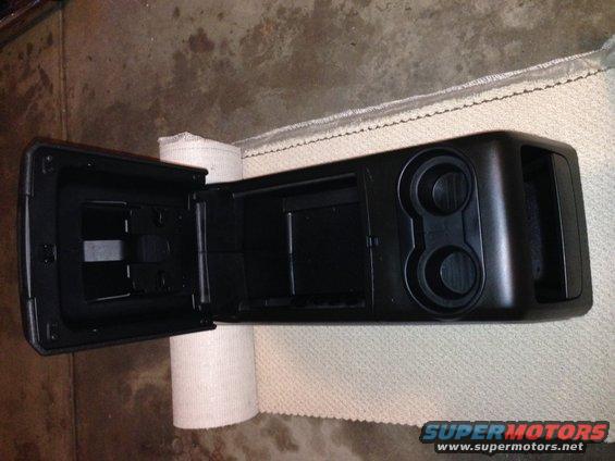 Black plastic center console with open storage compartment and two cup holders