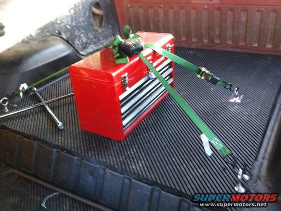 Red toolbox secured with green straps in a truck bed