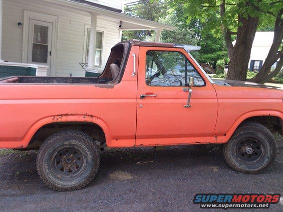 Side view of an orange SUV with a removable top, parked outside a house