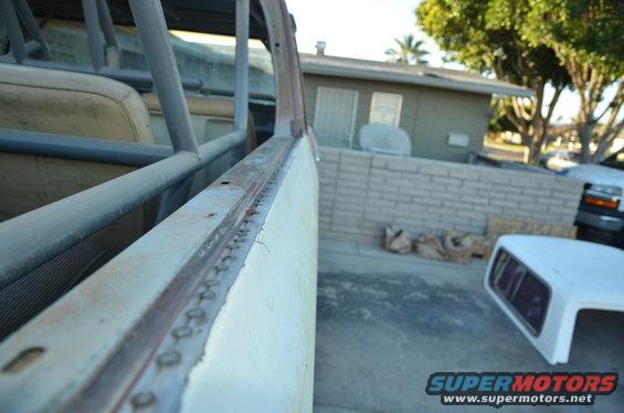Interior roll cage and seats of a vehicle under repair, with a white camper shell and a dark truck visible outside