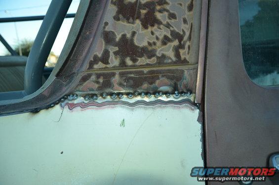 Close-up of welding on a vehicle's body panel, showing rust and repair work