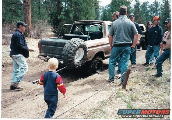 Brown Ford Bronco stuck in mud, spare tire mounted on rear, roll cage visible