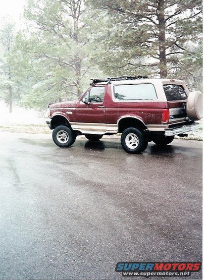 Red and tan 1996 Ford Bronco parked on wet asphalt with trees in the background
