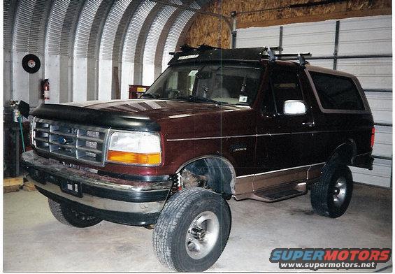 Maroon Ford Bronco with roof rack and aftermarket wheels parked inside a garage