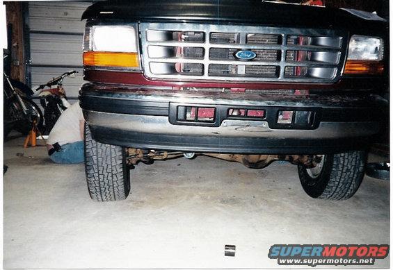 Front view of a maroon Ford truck with a chrome grille. Tires and undercarriage are visible