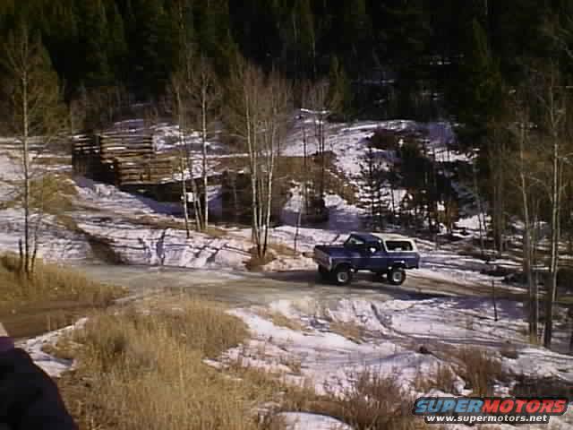 1996 Ford Bronco driving on a dirt road with snow and trees