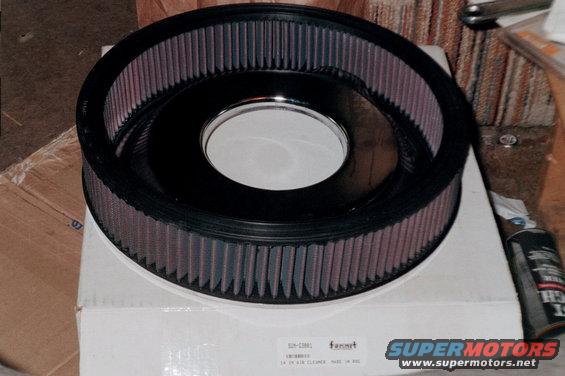 Black air filter with purple media sits on a white box with text. A can of spray is to the right