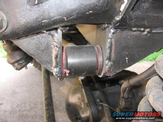 Close-up of a black suspension bushing with red trim, attached to a black metal frame with visible welds