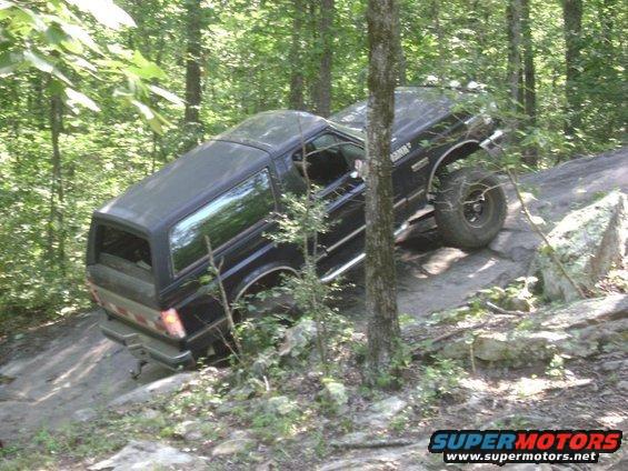 Black 1988 Ford Bronco climbing over rocks on a wooded trail