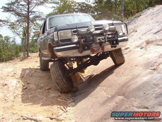 Dark gray Ford Bronco with a winch and off-road lights climbing a rocky incline