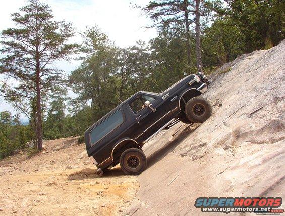 Black Ford Bronco climbing a steep, rocky incline with trees in the background