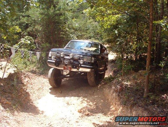Black SUV with off-road modifications on a dirt trail, front grille and lights visible