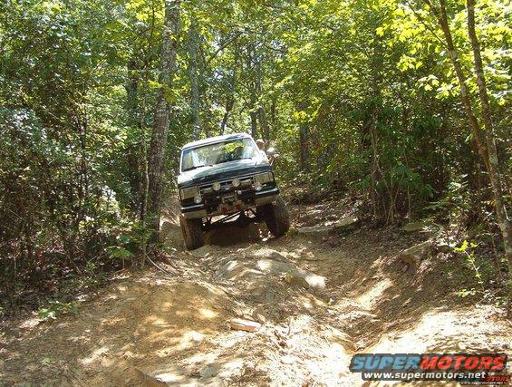 dark-colored SUV climbing a steep, rocky dirt path in a wooded area