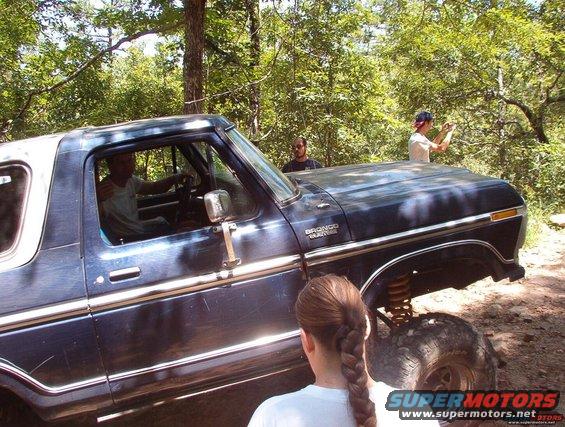 Dark blue Ford Bronco with white top, side view, lifted suspension