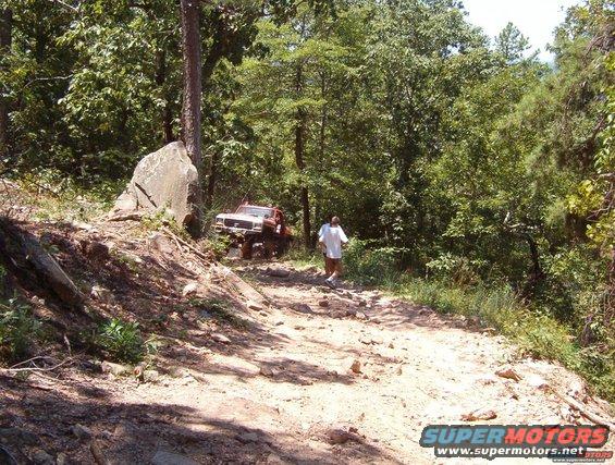 guy walking near a red off-road SUV on a rocky trail in the woods