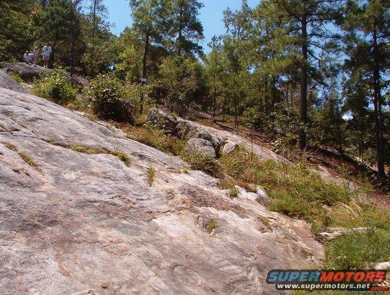 Rocky hillside with trees and a few people standing on top