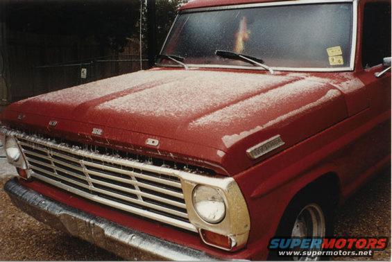 Front view of a red 1967 Ford F-100 with snow on the hood and grille
