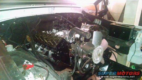 Engine with chrome headers and black valve covers, visible fan and carburetor
