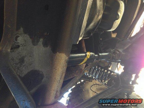 Underside view of a driveshaft with a yellow marker and suspension components