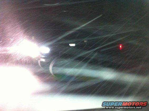 Dark SUV driving in snow with headlights on