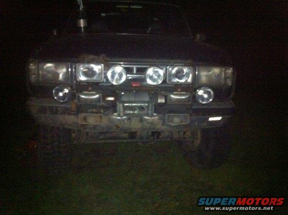Dark-colored Ford Bronco front end with multiple auxiliary lights and a winch mounted on the bumper